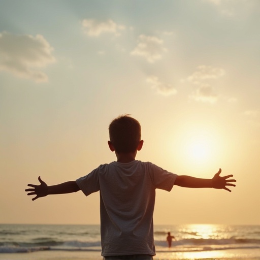 Boy stands on the beach at sunset with arms open wide. Ocean waves in the background. Sky filled with clouds. Sun setting on the horizon.