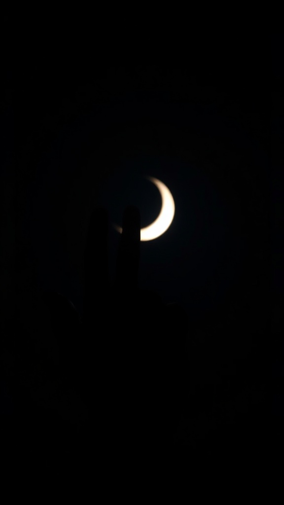 A silhouette of a hand placed against a bright crescent moon in a dark night sky.