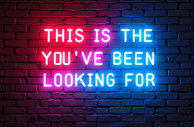 A neon sign on a brick wall with the message 'THIS IS THE YOU'VE BEEN LOOKING FOR' in vibrant pink and blue lights.