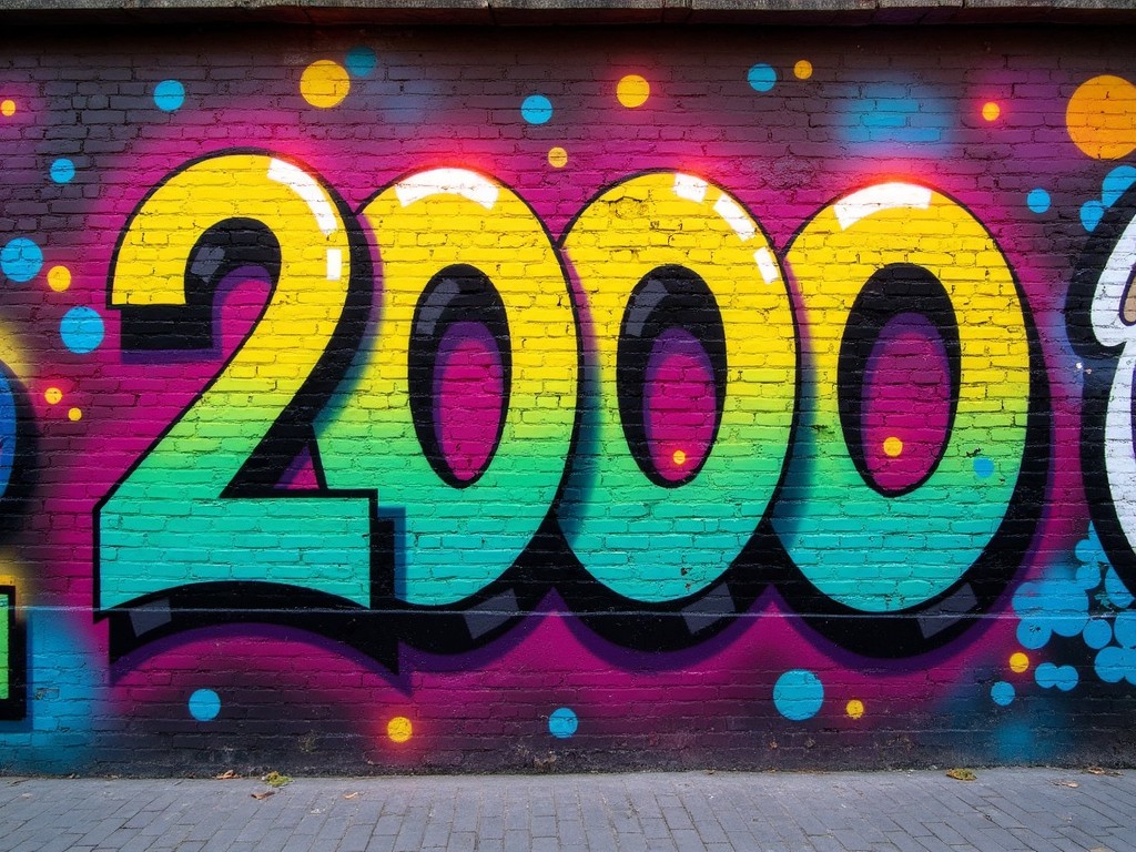 The image features a vibrant graffiti mural depicting the number '2000'. The mural is painted on a brick wall, using a bright color palette that includes green, yellow, pink, and blue. The large numbers are styled with a gradient effect, making them pop against the darker background. The surrounding splashes of color add to the mural's lively and energetic feel. This art piece captures the essence of urban creativity and may evoke a sense of nostalgia for the year 2000.