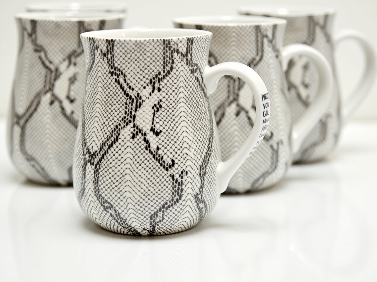 This image features a collection of ceramic mugs with a unique snake pattern. The mugs are arranged in a line, showcasing their design from a slightly overhead perspective. Each mug is similar in shape but distinct in pattern, providing an interesting visual effect. The colors are primarily black and white, giving them a modern and stylish look. The bright lighting highlights the texture of the mugs, emphasizing their ceramic finish and unique pattern.