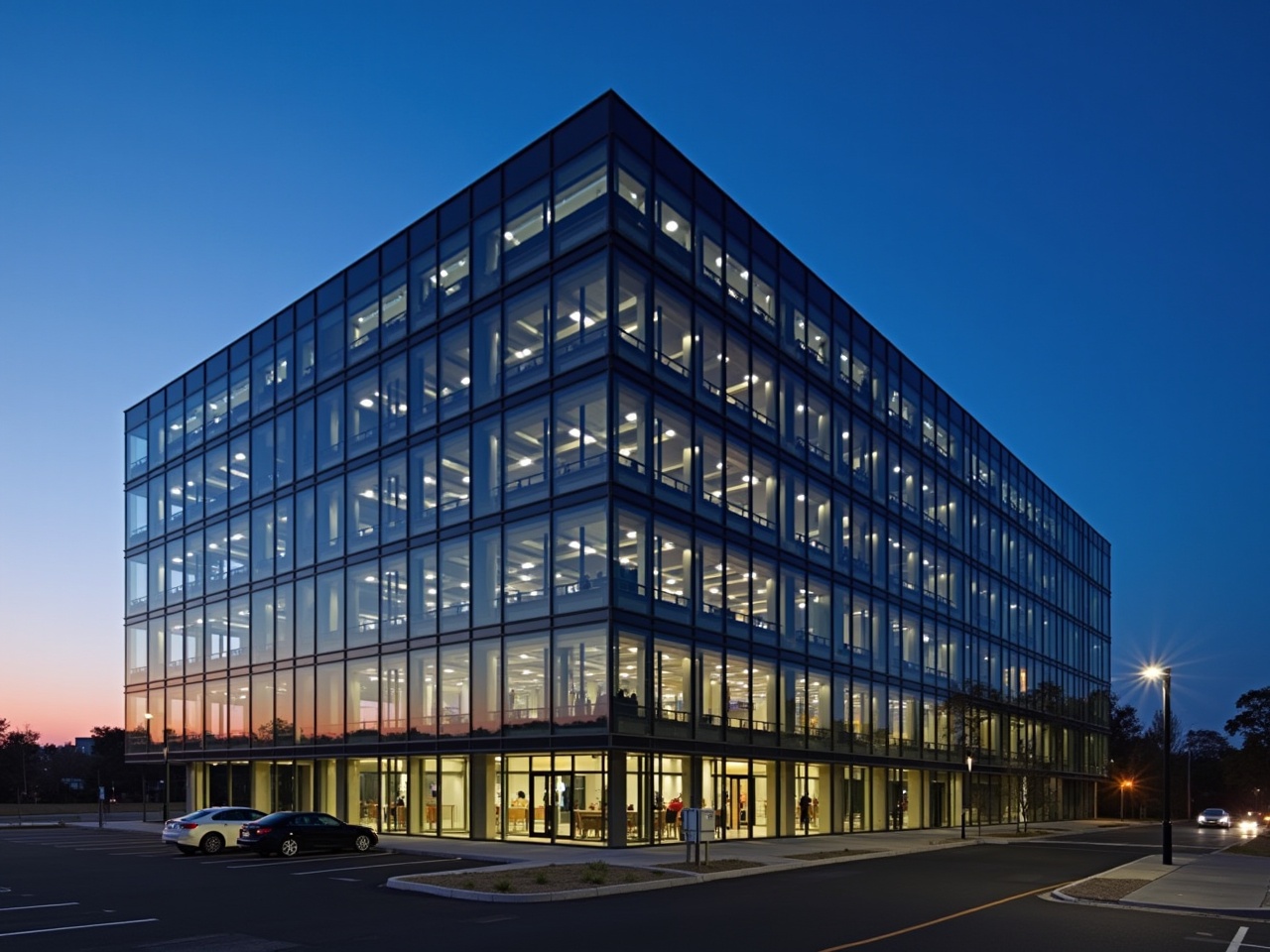 A modern glass office building illuminated at evening with a clear blue sky, showcasing urban architecture.