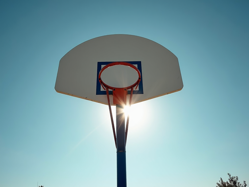 A basketball hoop is silhouetted against a bright, clear blue sky with the sun shining through the net.