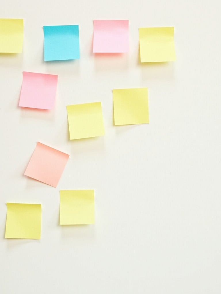 Sticky notes in various colors stick to a white surface. Notes are yellow pink and blue. Arrangement is casual and random. Empty space on the right.