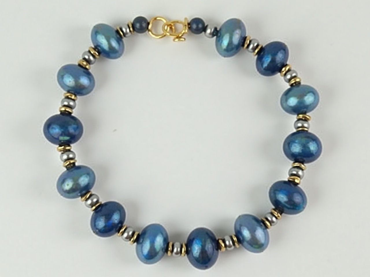 This image features a beautifully crafted necklace made of mother of pearl beads. There are a total of fifty-six beads, with every fourteenth bead colored a vibrant blue. The necklace is adorned with gold and silver accents, enhancing its elegance. The lighting captures the glossy surface of the beads, making them shine. It's a perfect accessory for women looking to add a touch of color to their outfits.