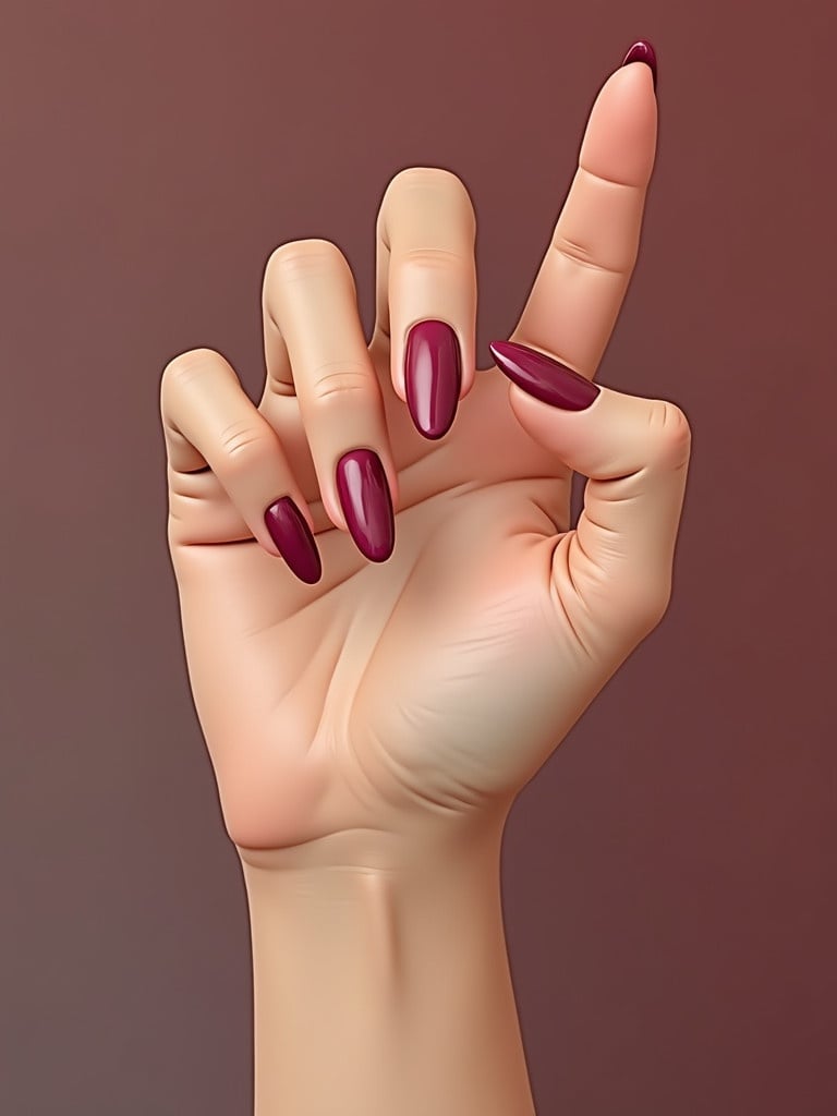 Close-up view of a female hand displaying elegantly manicured nails. The hand shows a variety of nail shapes and a rich burgundy color. The gesture is playful and stylish. Background is softly blurred to highlight the hand.