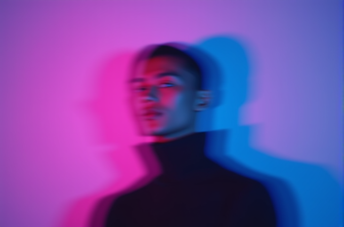 A person in a black turtleneck is blurred with vibrant pink and blue lighting creating a dreamy effect.